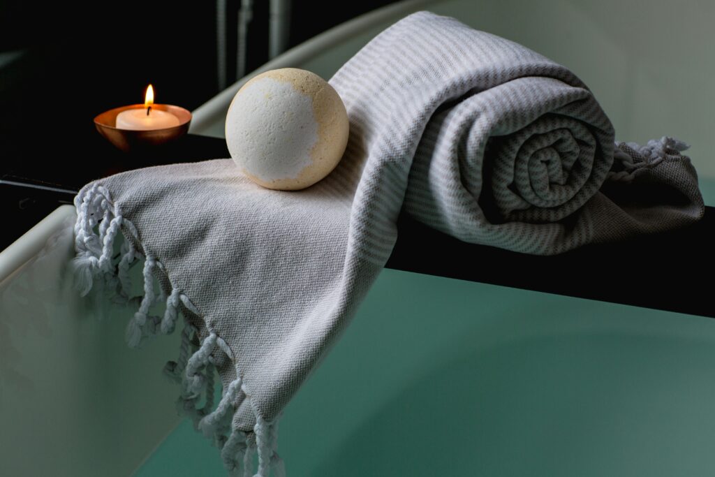 Serene spa scene with a lit candle, bath bomb, and towel on the bathtub edge.